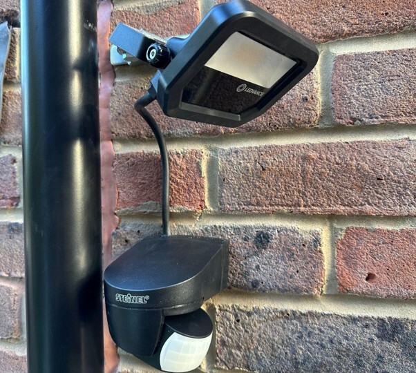 Outdoor security light installation with motion sensor mounted on a brick wall.